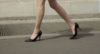Жінка йде по вулиці у чорних лакованих туфлях на шпильці.