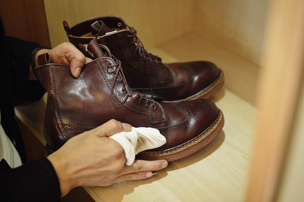 Чоловік полірує шкіряні чоботи коричневого кольору.