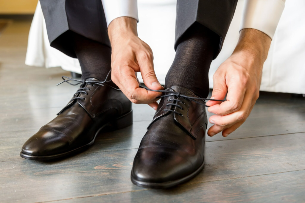 Mężczyzna zawiązuje eleganckie buty cienkimi, okrągłymi, woskowanymi sznurówkami.