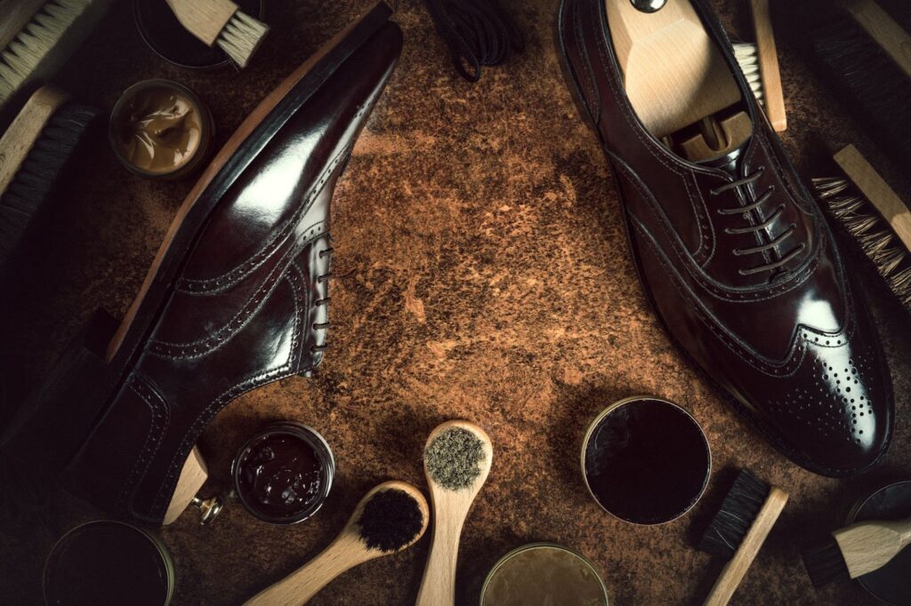 Чоловічі елегантні чорні лаковані туфлі лежать між щітками та кремами, призначеними для чищення та полірування.
