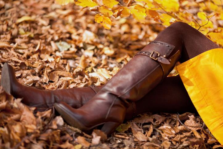 Дівчина у високих коричневих чоботах на каблуку лежить на опалому листі.