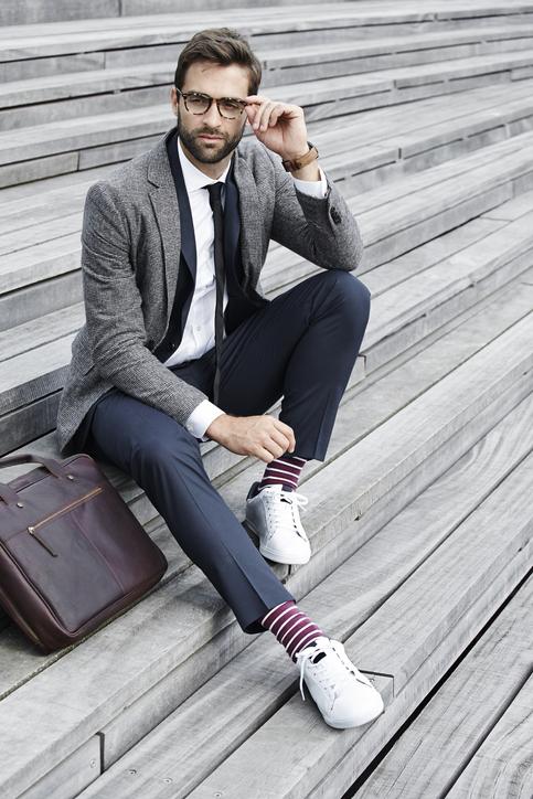 Чоловік сидить у білих скікерсах і у бордових шкарпетках з білими смужками.