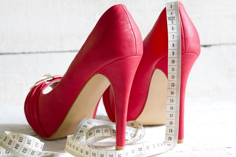 Червоні туфлі на шпильці, поставлені задом і на них лежить сантиметр.