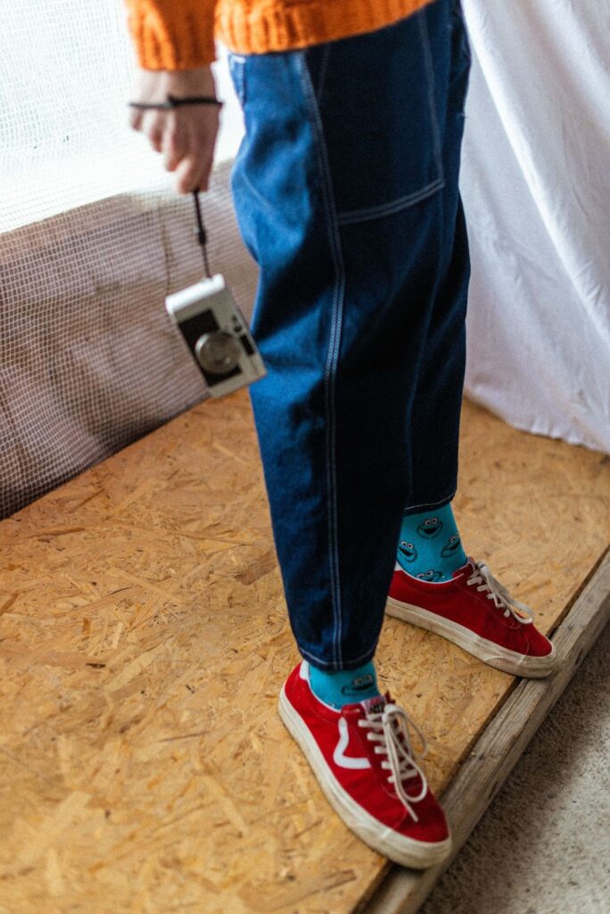 Чоловік у кольорових високих шкарпетках і червоних кедах тримає цифровий фотоапарат.