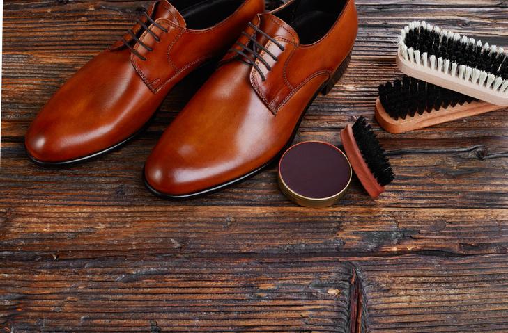 Шкіряне коричневе взуття, крем та щітки для полірування взуття лежать на дерев'яній підлозі.
