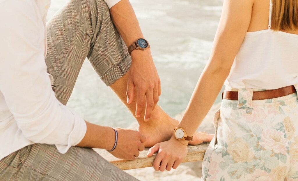 Чоловік з жінкою, у яких на руках висять дерев'яні годинники, стоять на березі моря.