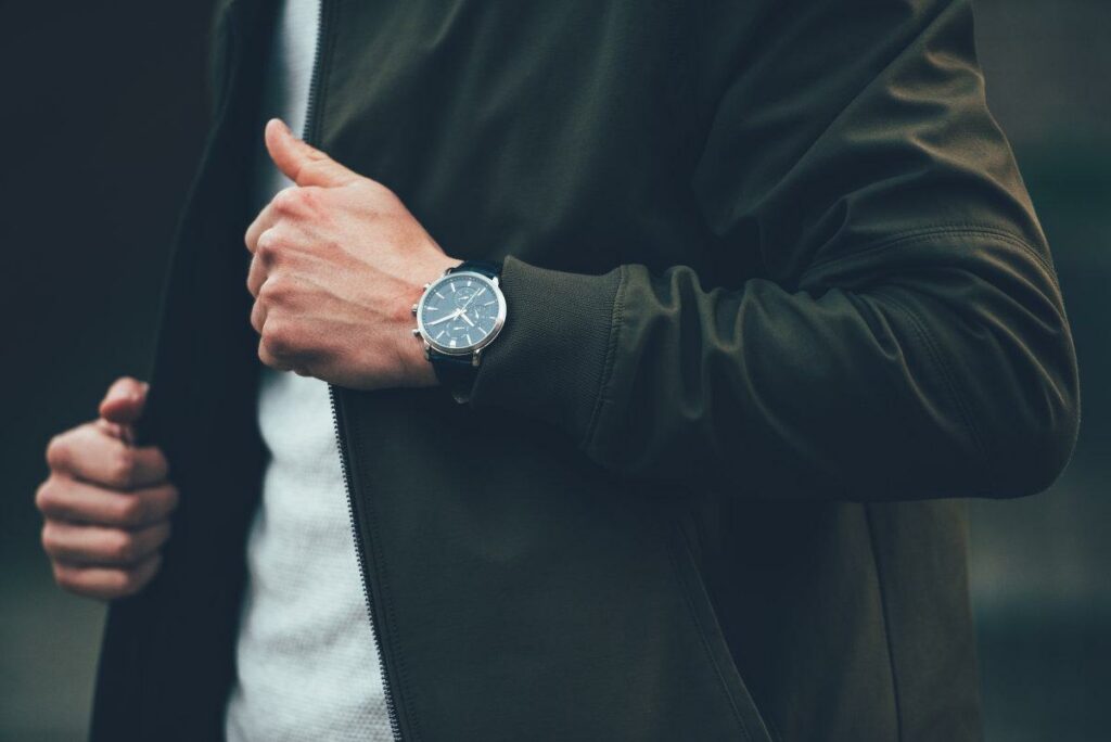 Чоловік з годинником на руці тримає за комір куртку.