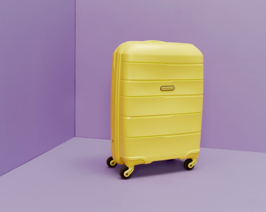 Жовта валіза бренду Puccini стоїть на фіолетовому фоні.