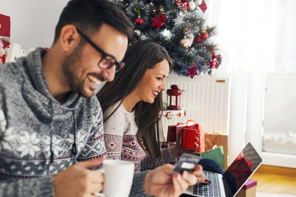 Жінка і чоловік сидять біля новорічної ялинки і дивляться у ноутбук.