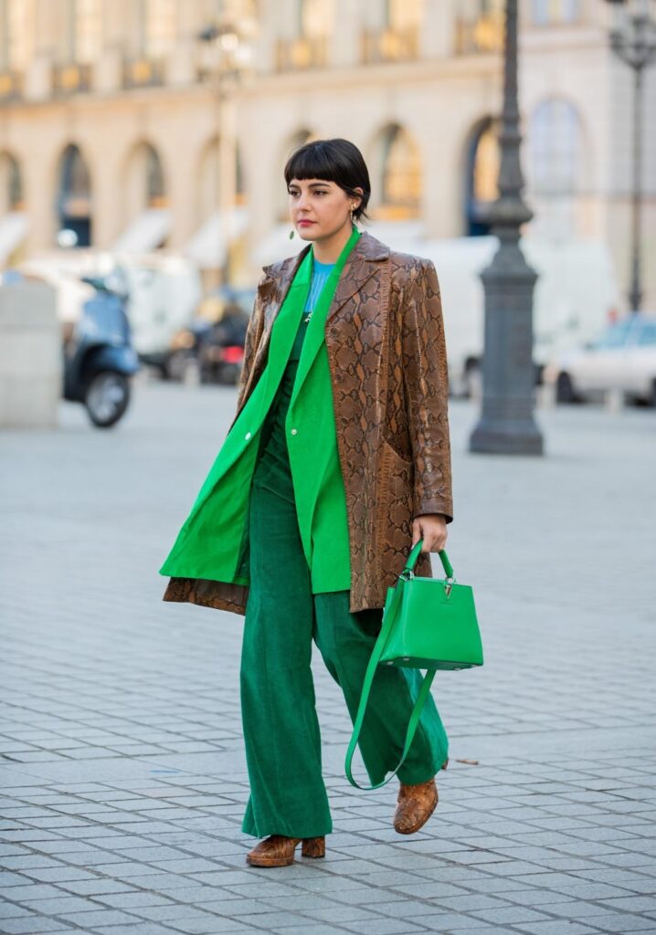 Жінка у зеленому total look і коричневою курткою і ботильйонами на каблуку-стовпчику зі зміїним принтом.