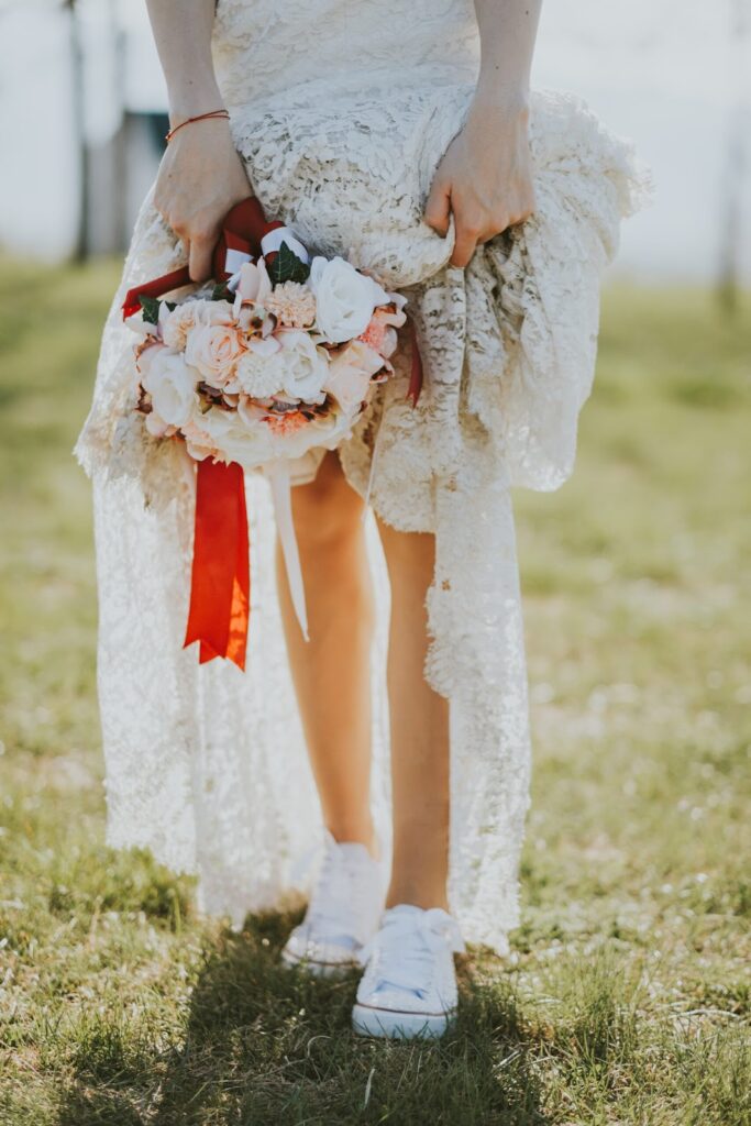 Жінка у весільній сукні в стилі бохо з букетом квітів у руці та білих кедах нижче щиколотки