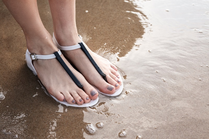 Жіночі ноги у гумових босоніжках на піщаному пляжі.